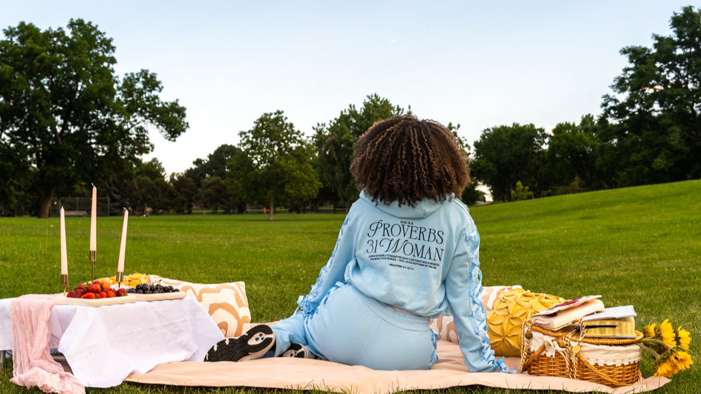 Person sitting on a picnic blanket with a basket and food in a park